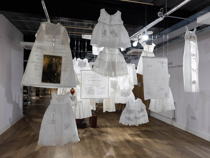 Image from the installation from the back: white garments hung from the ceiling