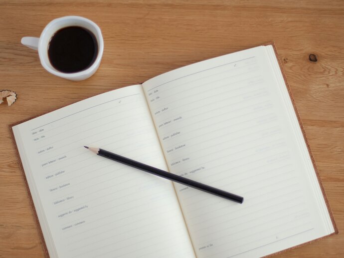 An open diary on a desk with a cup of coffee and a pencil