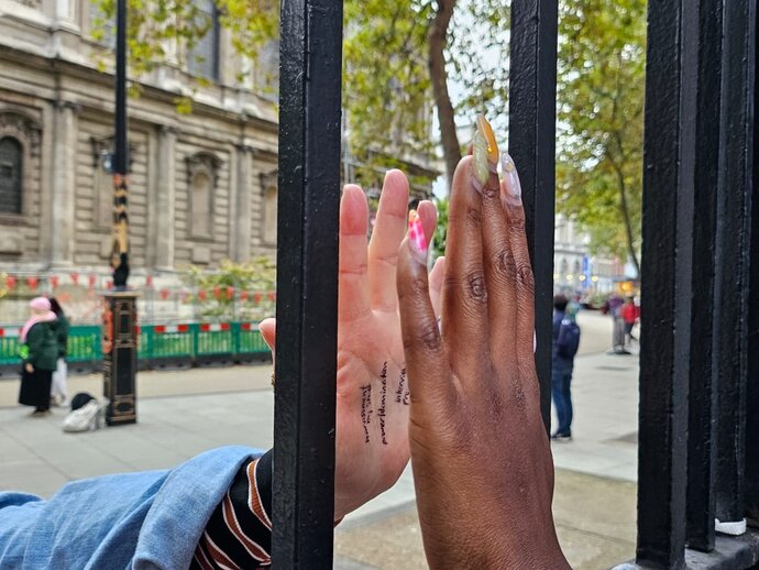 A Black person and a white person touching their hands to either side of a glass window