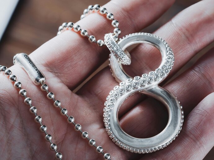 A necklace in the shape of the infinity symbol made out of tentacles, held in someones hand