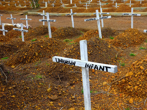 A photo of a graveyard marked by white crosses reading "unknown infant"