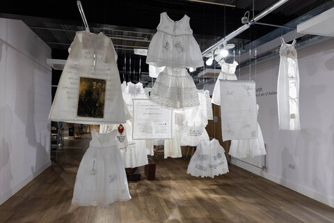 Image from the installation from the back: white garments hung from the ceiling