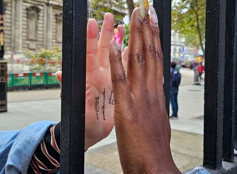 A Black person and a white person touching their hands to either side of a glass window