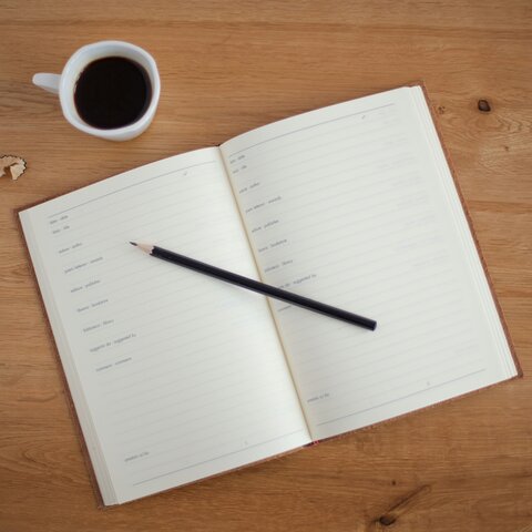 An open diary on a desk with a cup of coffee and a pencil